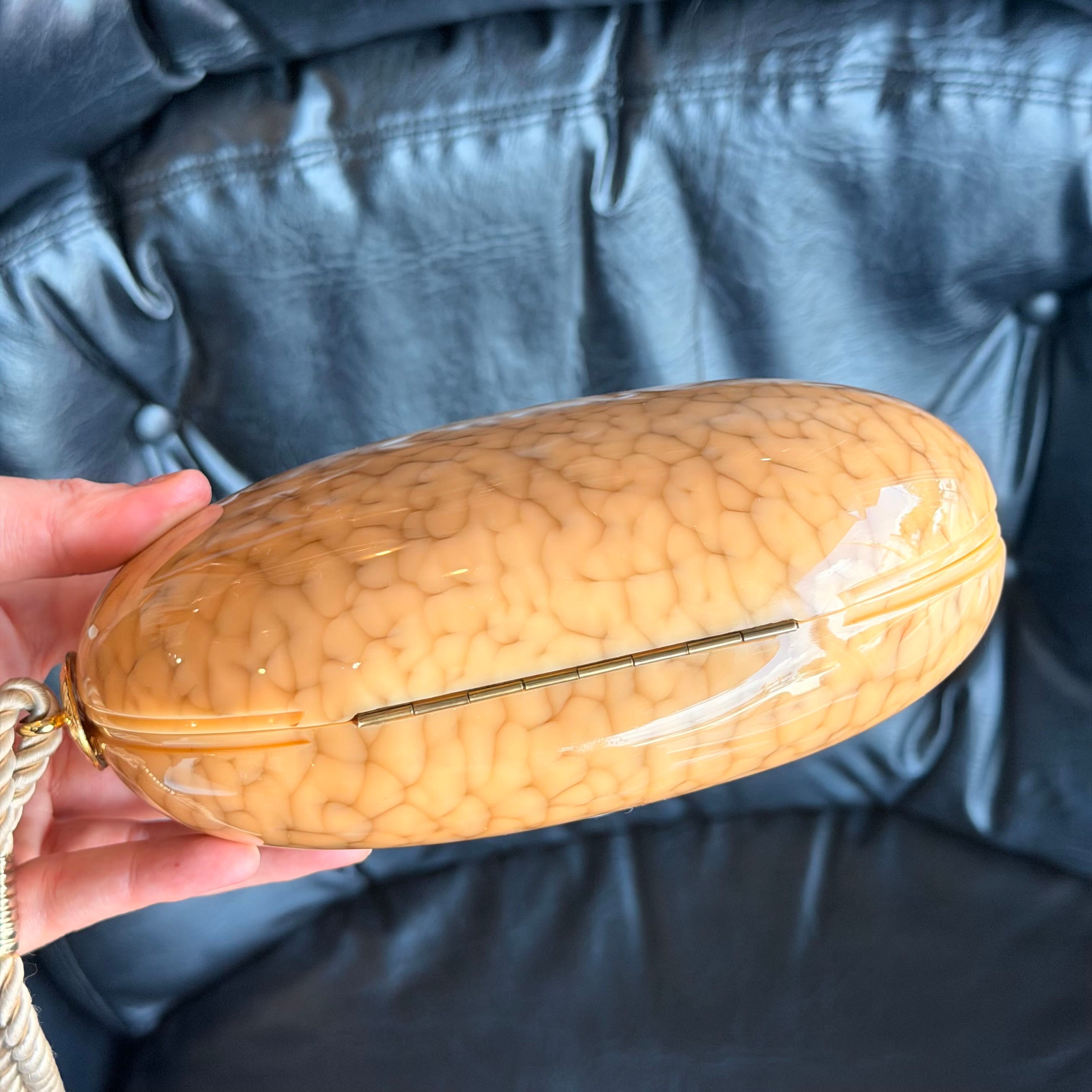 Hand holding a textured beige clutch against a blue background