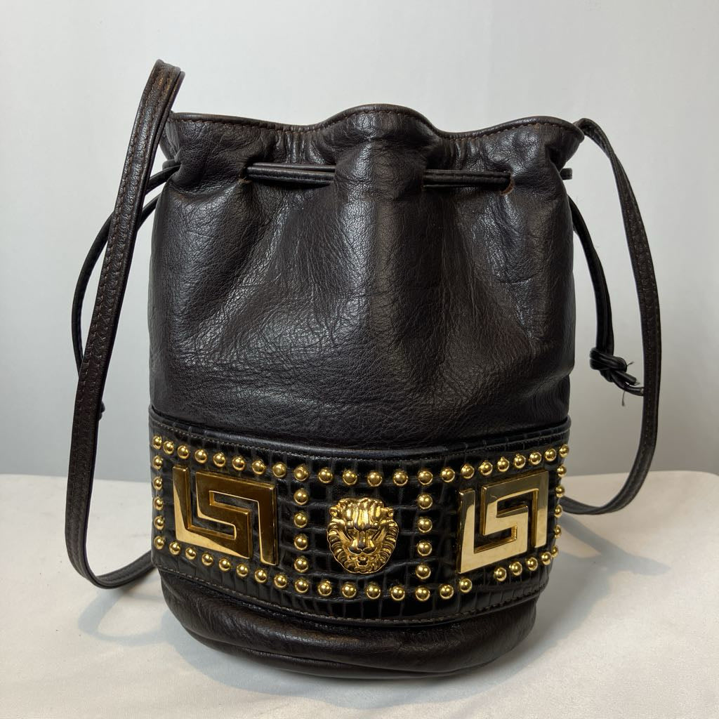 Black leather bucket bag with gold studded detailing on a light gray background