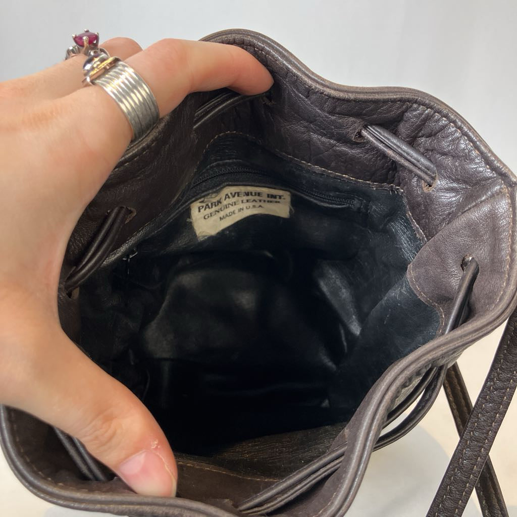 Hand opening a brown leather bag with a visible brand label on a light background