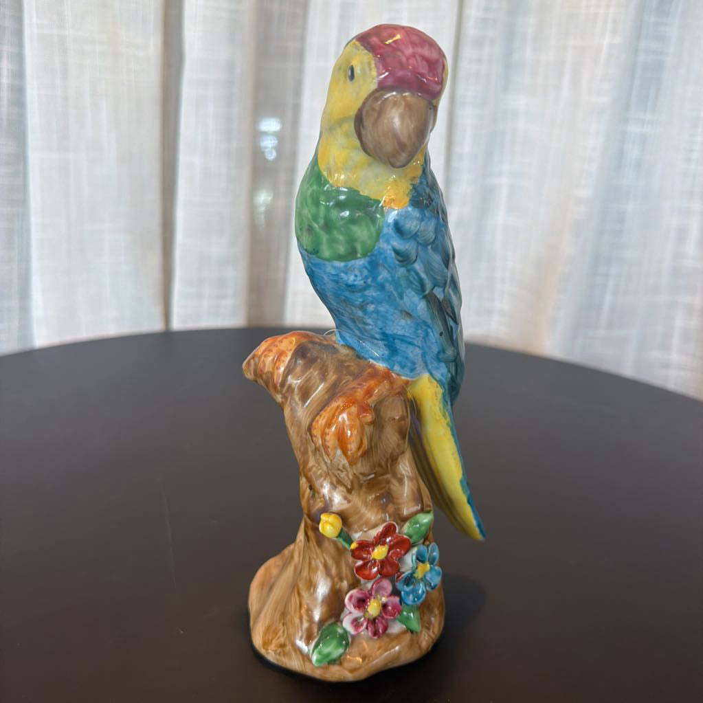 Colorful parrot figurine on a branch with flowers against a white curtain background