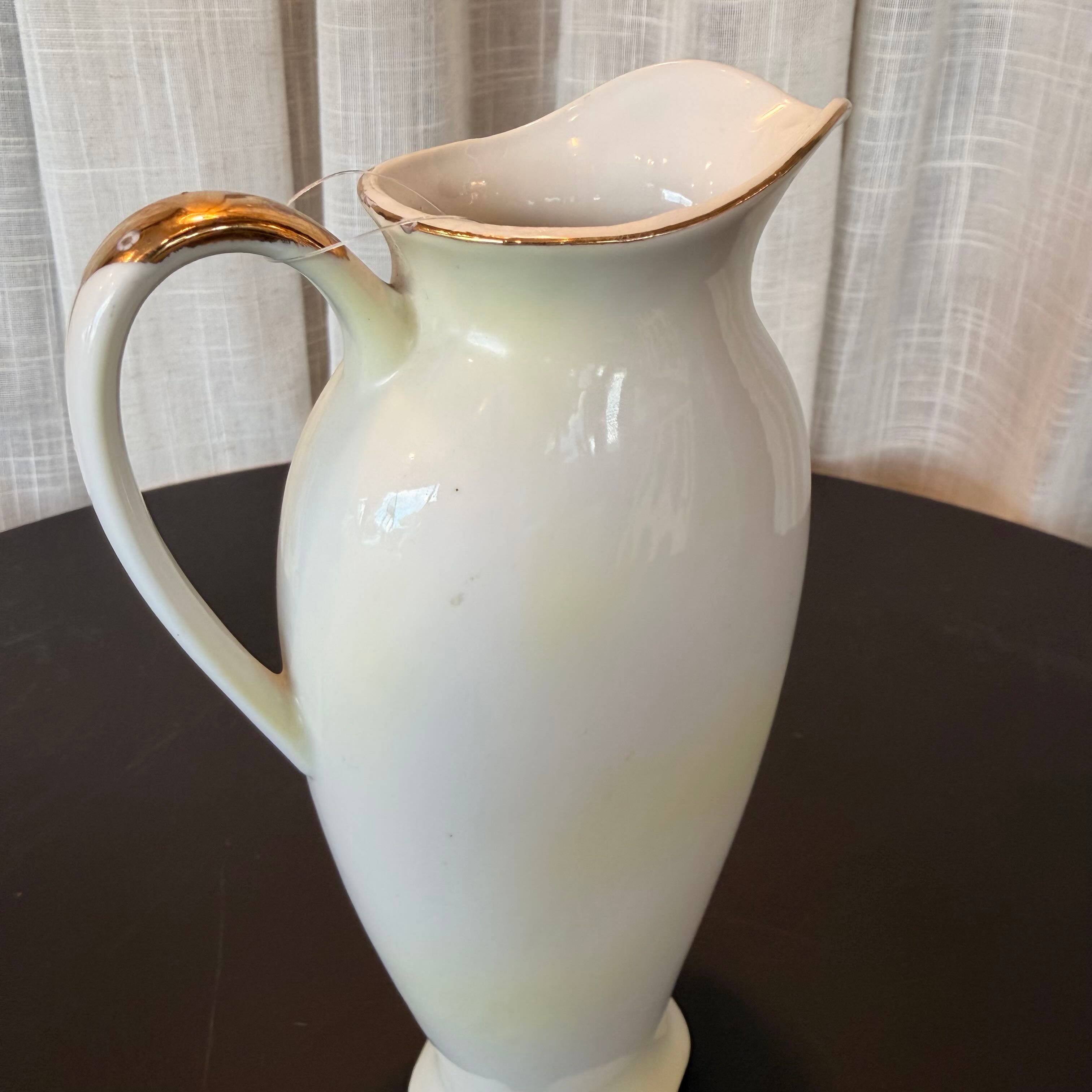 White ceramic pitcher with gold accents on a dark surface