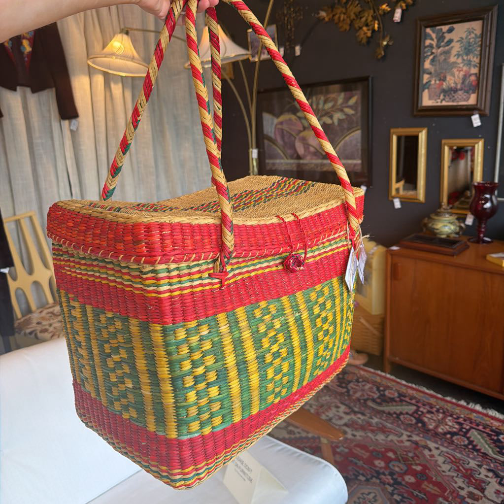 Colorful woven basket with red, yellow, and green patterns held by a person in an indoor setting.