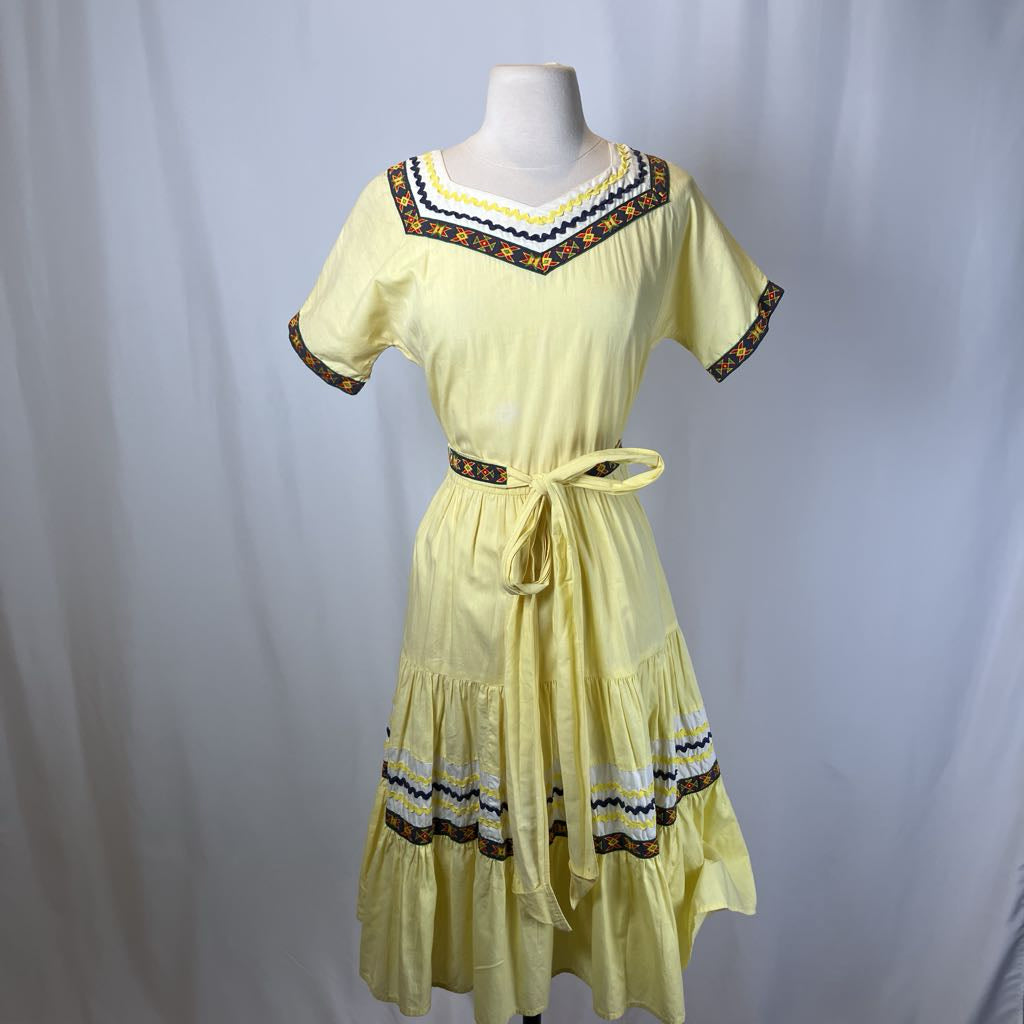Yellow dress with decorative patterns on a mannequin against a plain background