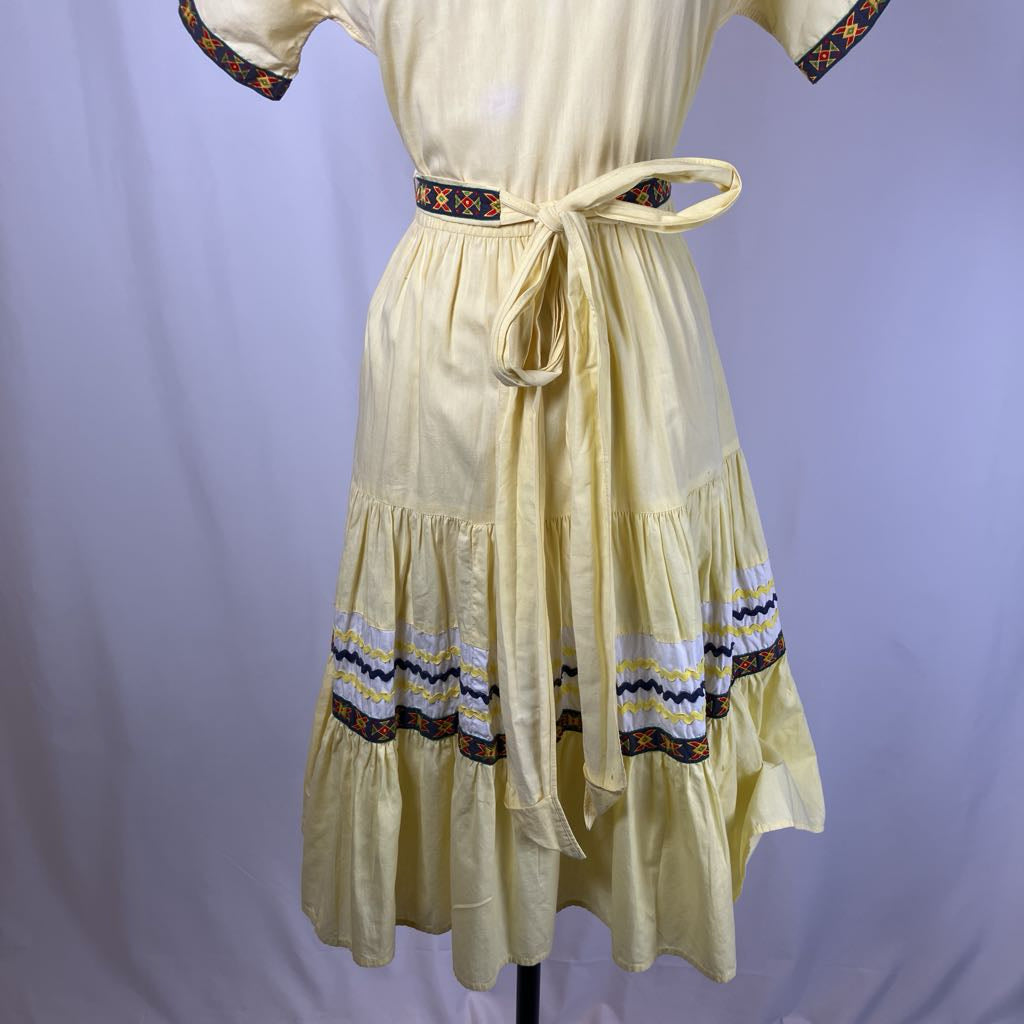 Light yellow dress with decorative trim on a mannequin against a plain background