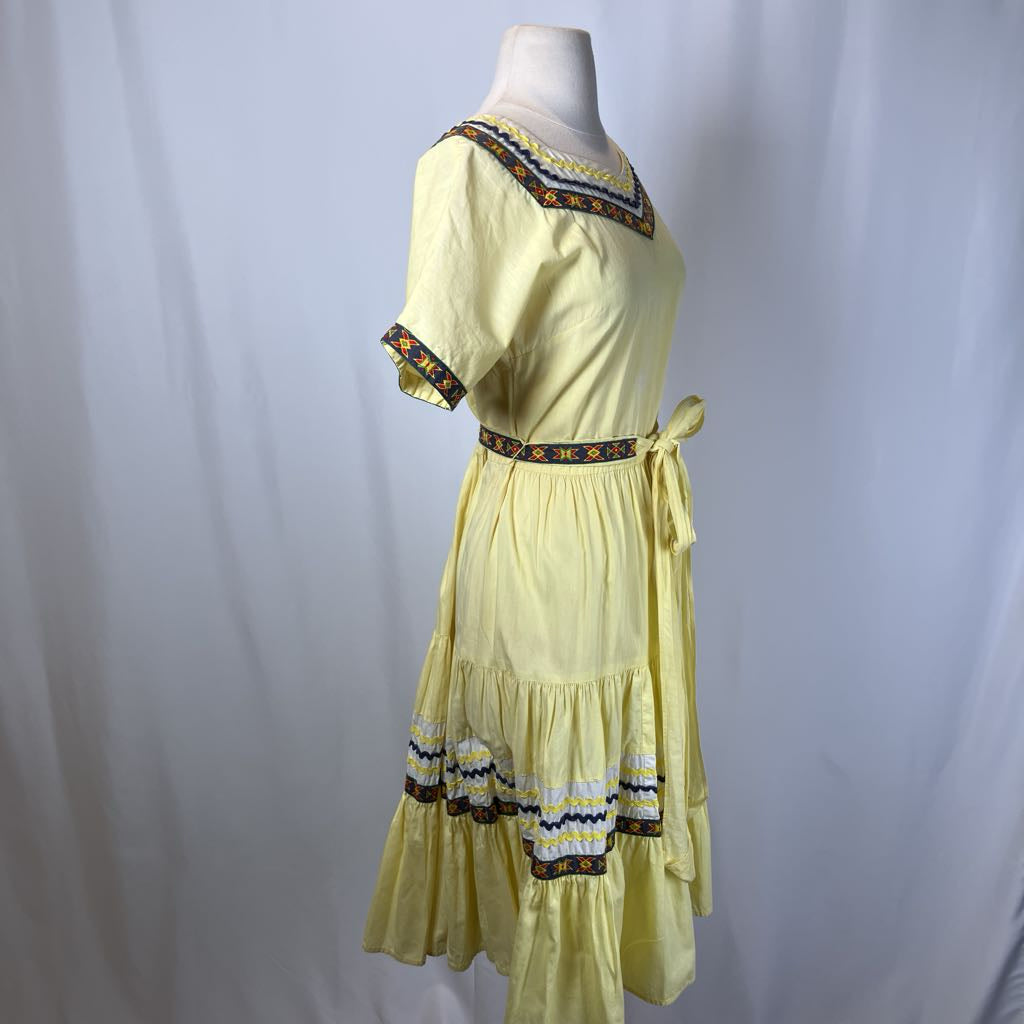 Light yellow dress with decorative patterns on a mannequin against a plain background