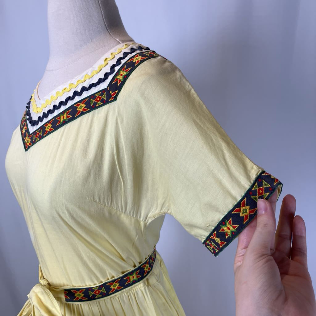 Mannequin wearing a light yellow dress with colorful embroidery on a plain background