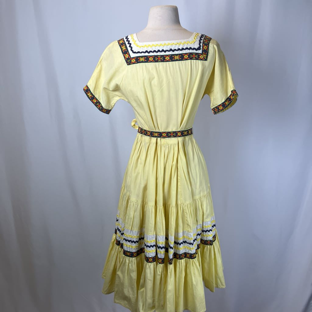 Yellow dress with decorative patterns on a mannequin against a plain background