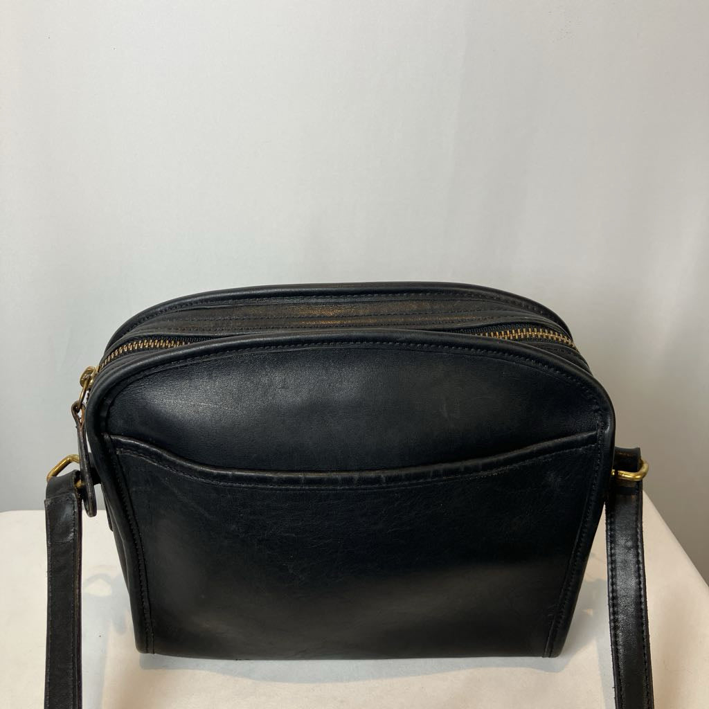 Black leather handbag with gold zipper on a light gray background