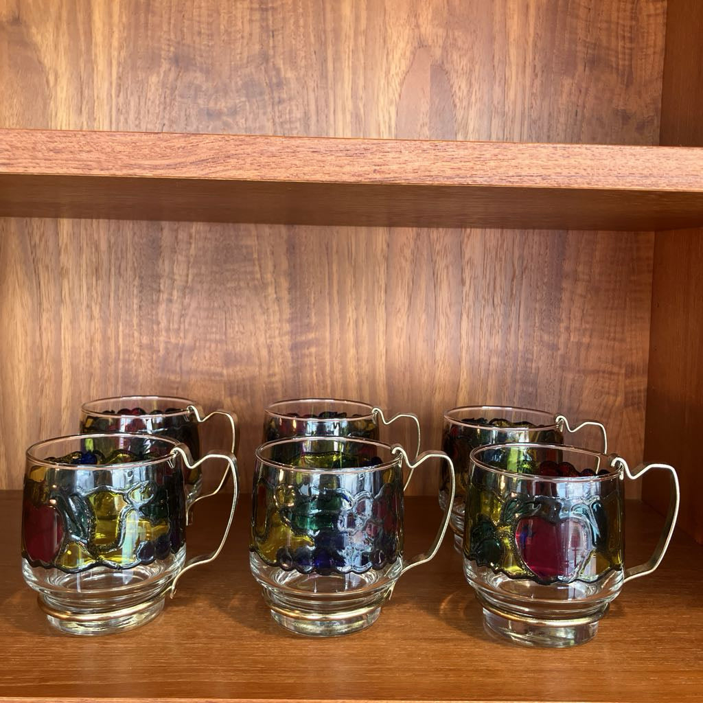 Set of six glass mugs with marble-like designs on a wooden shelf.