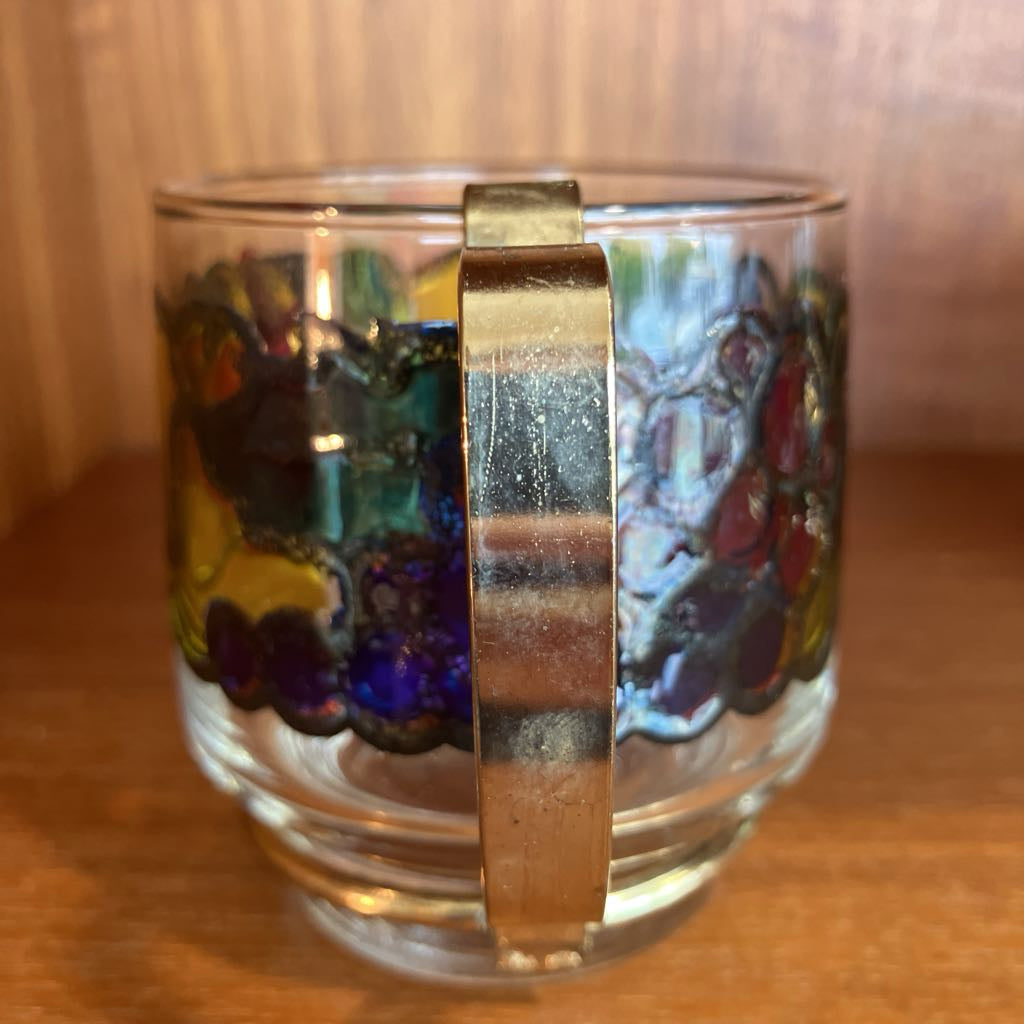 Glass mug with colorful design and a gold band on a wooden surface