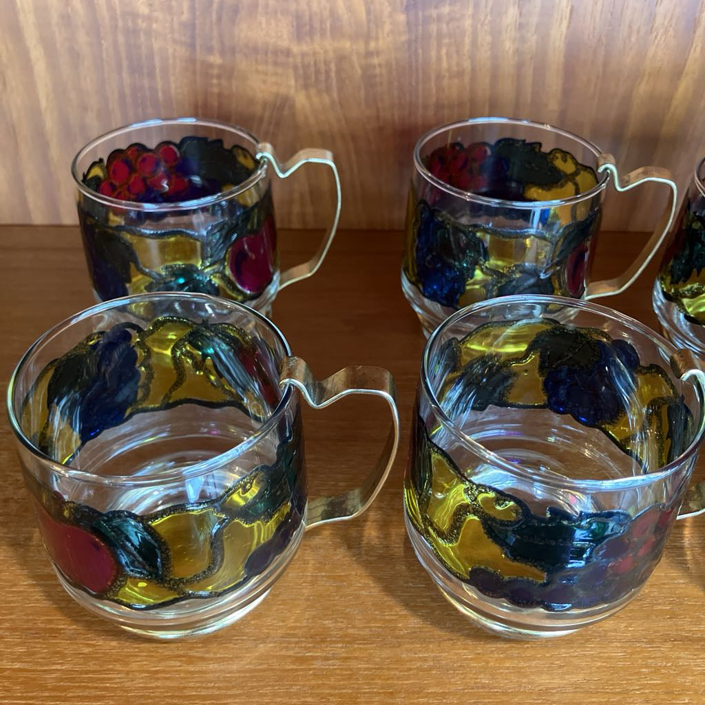 Set of four glass mugs with colorful designs on a wooden surface