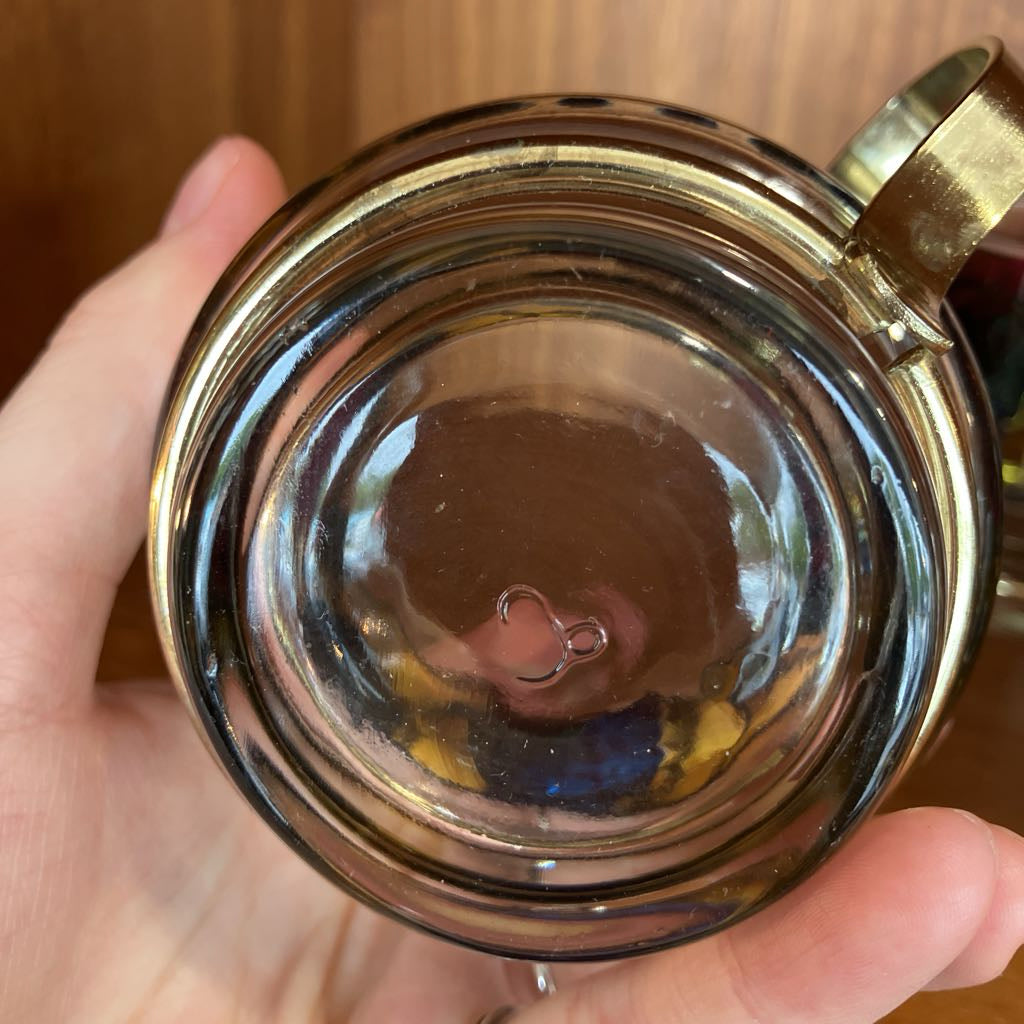 Hand holding a glass mug with a metal handle against a wooden background