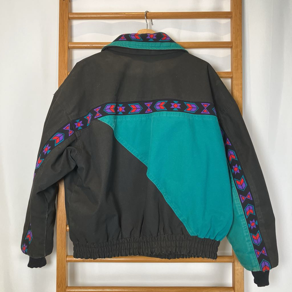 Black and teal jacket with colorful patterns on a wooden rack against a white wall