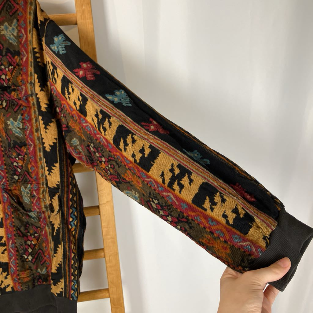 Hand holding a folded traditional rug with intricate patterns against a white wall.