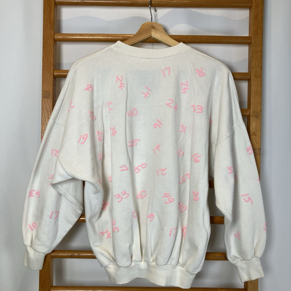 White sweatshirt with pink patterns on a wooden hanger against a wooden panel background