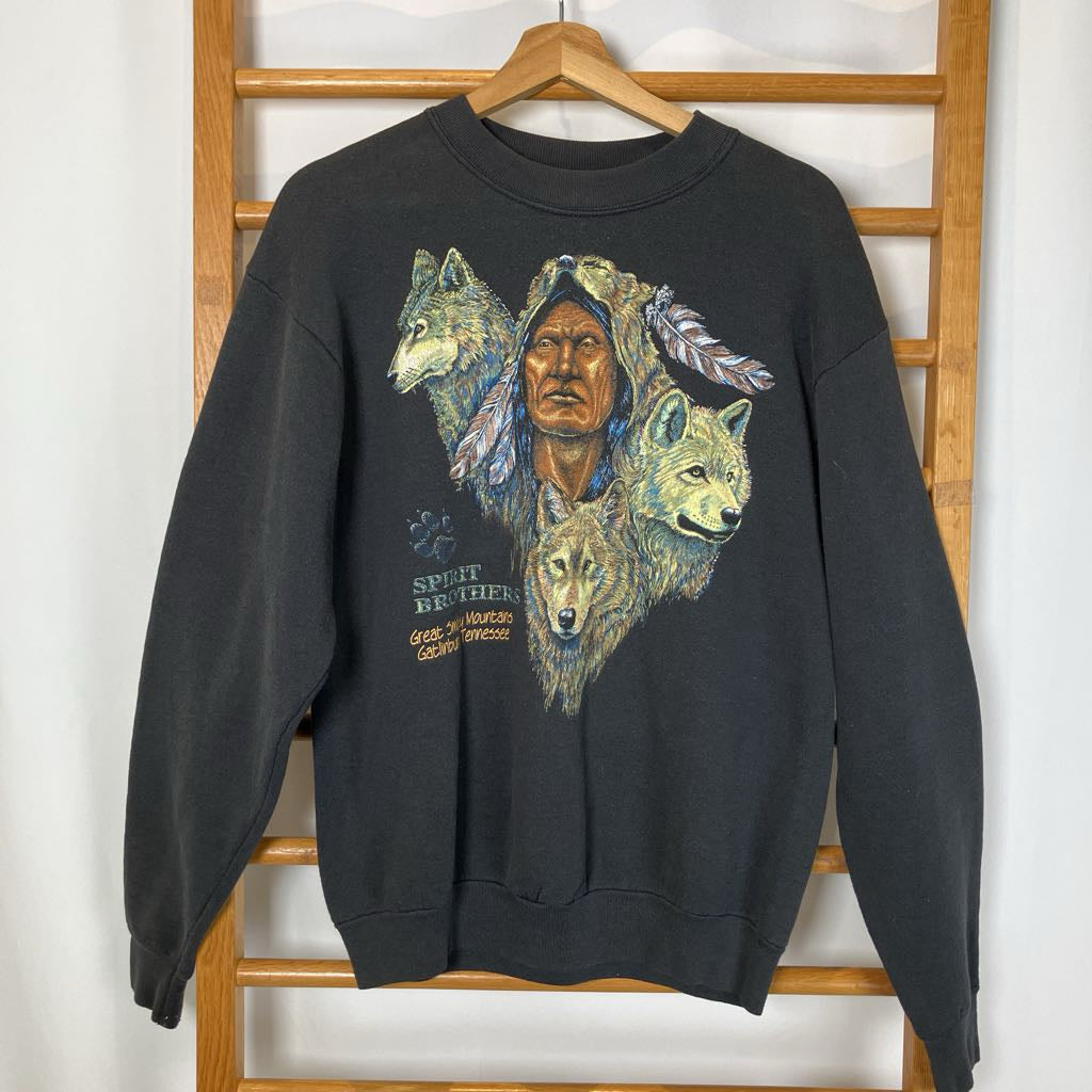 Black sweatshirt with a graphic of a Native American and wolves on a wooden rack.