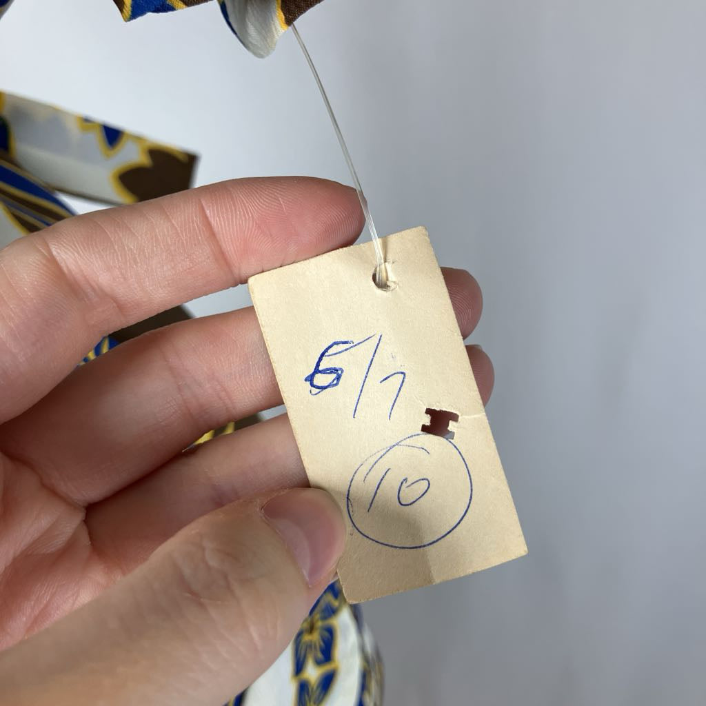 Hand holding a small brown tag with numbers written on it against a blurred background