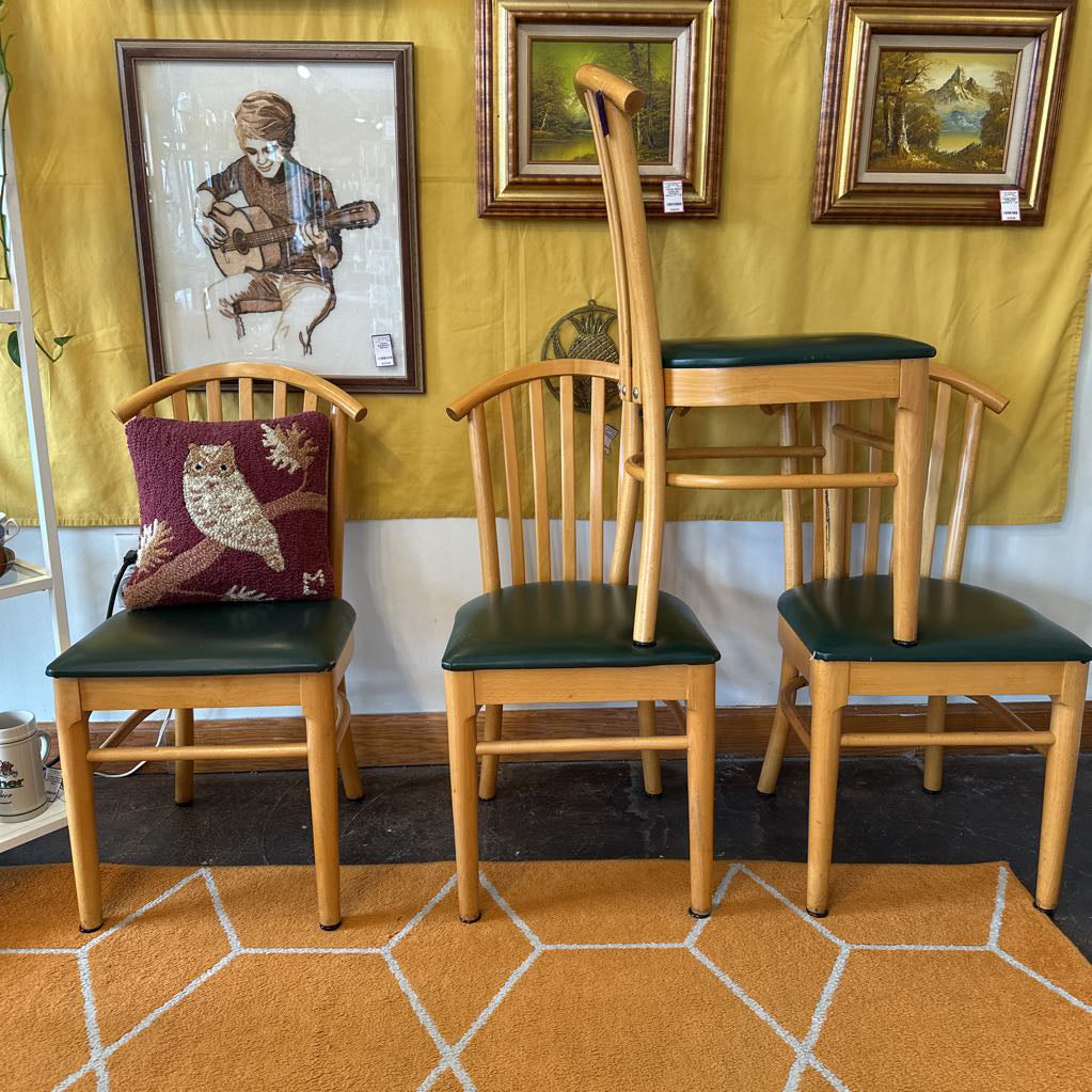 Set of wooden chairs with green seats against a yellow wall with framed pictures.