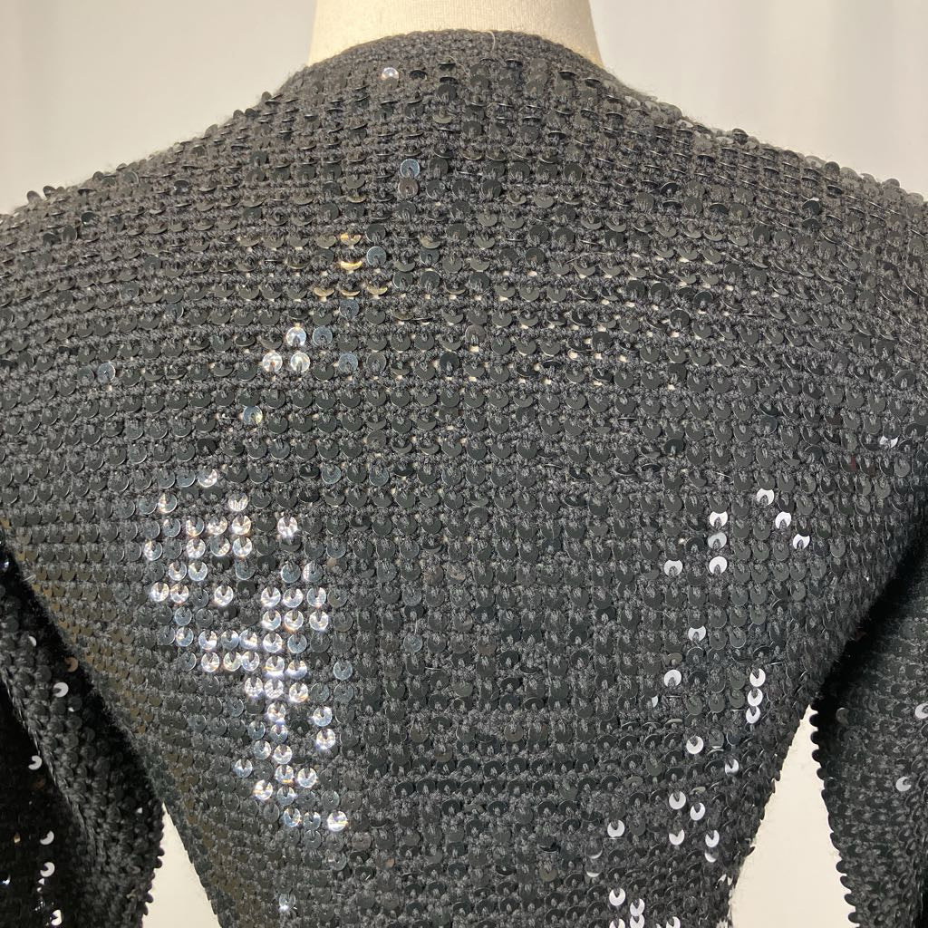 Black textured garment with silver sequins on a mannequin against a neutral background