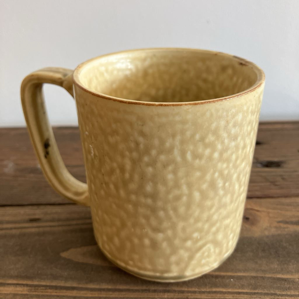 Beige ceramic mug with textured surface on a wooden surface