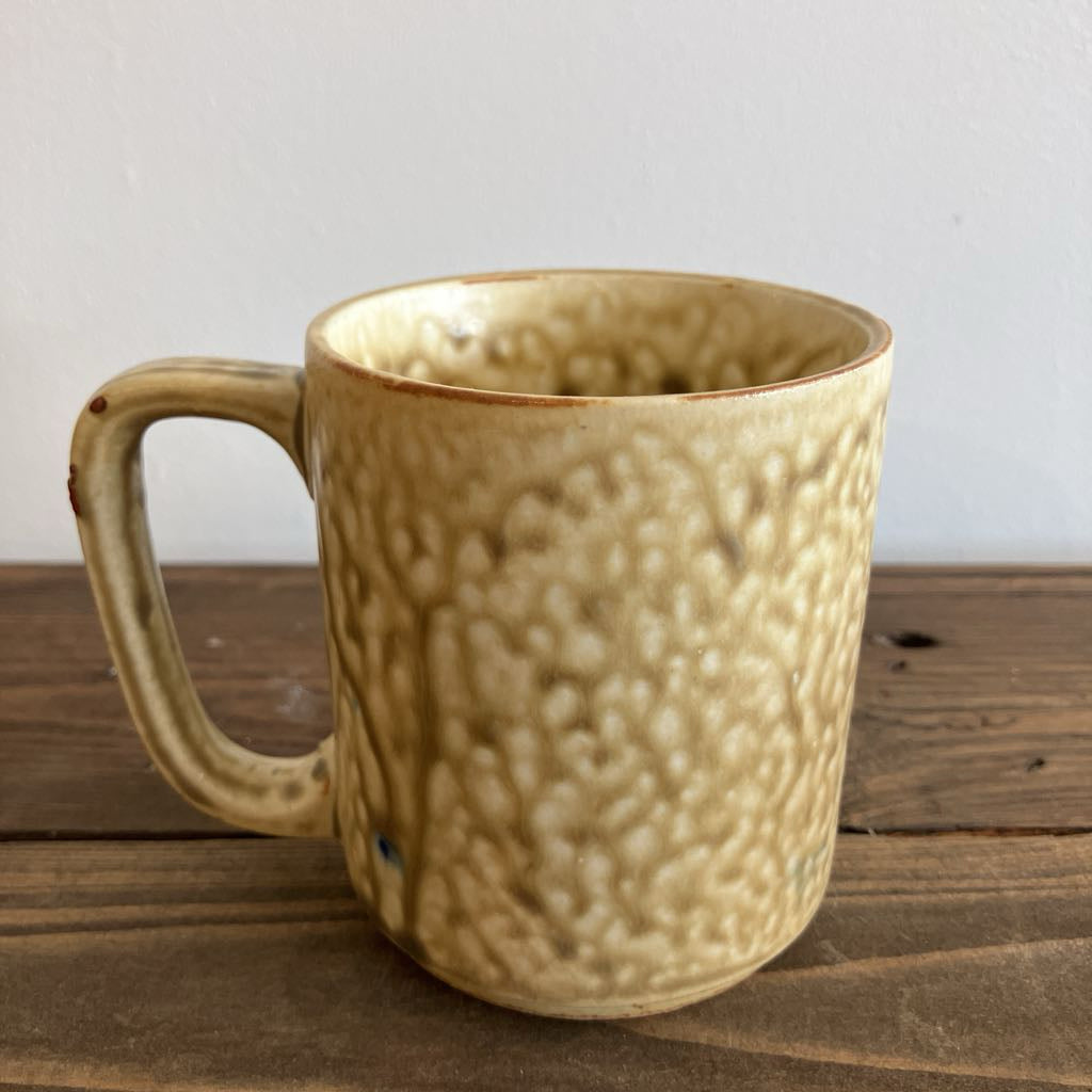 Beige ceramic mug with textured surface on a wooden surface