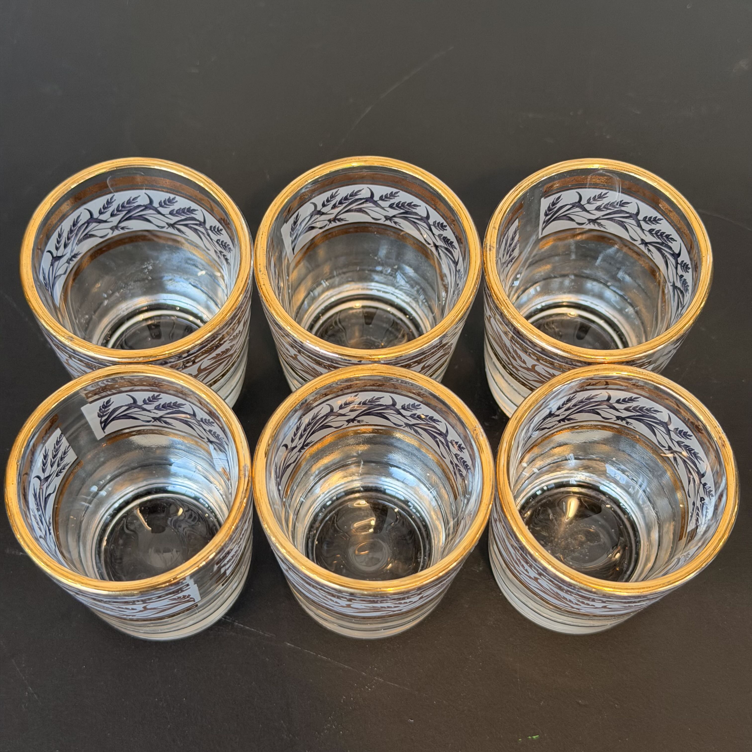 Set of six glass tumblers with gold rims on a dark surface
