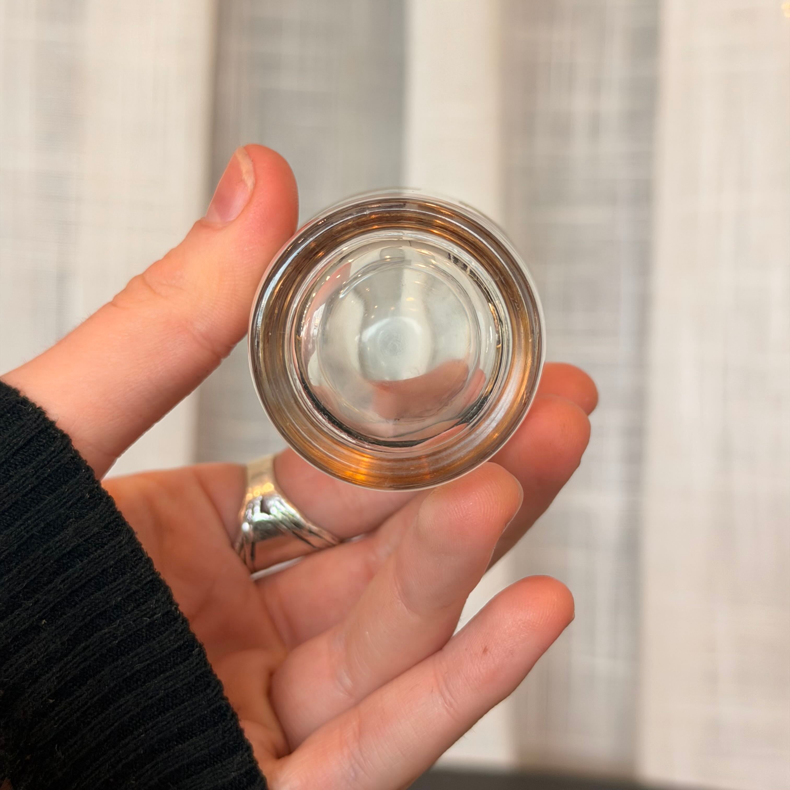 Hand holding a small transparent container with a metallic rim against a neutral background
