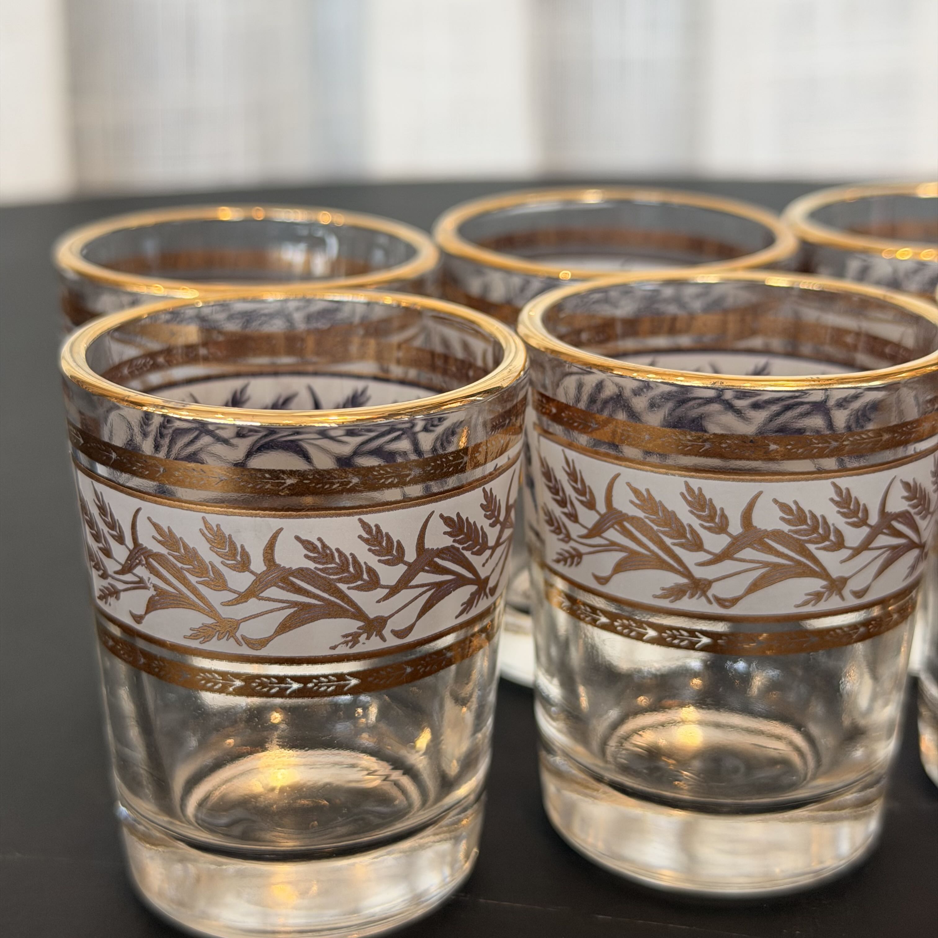 Set of clear glasses with gold and blue decorative patterns on a dark surface.