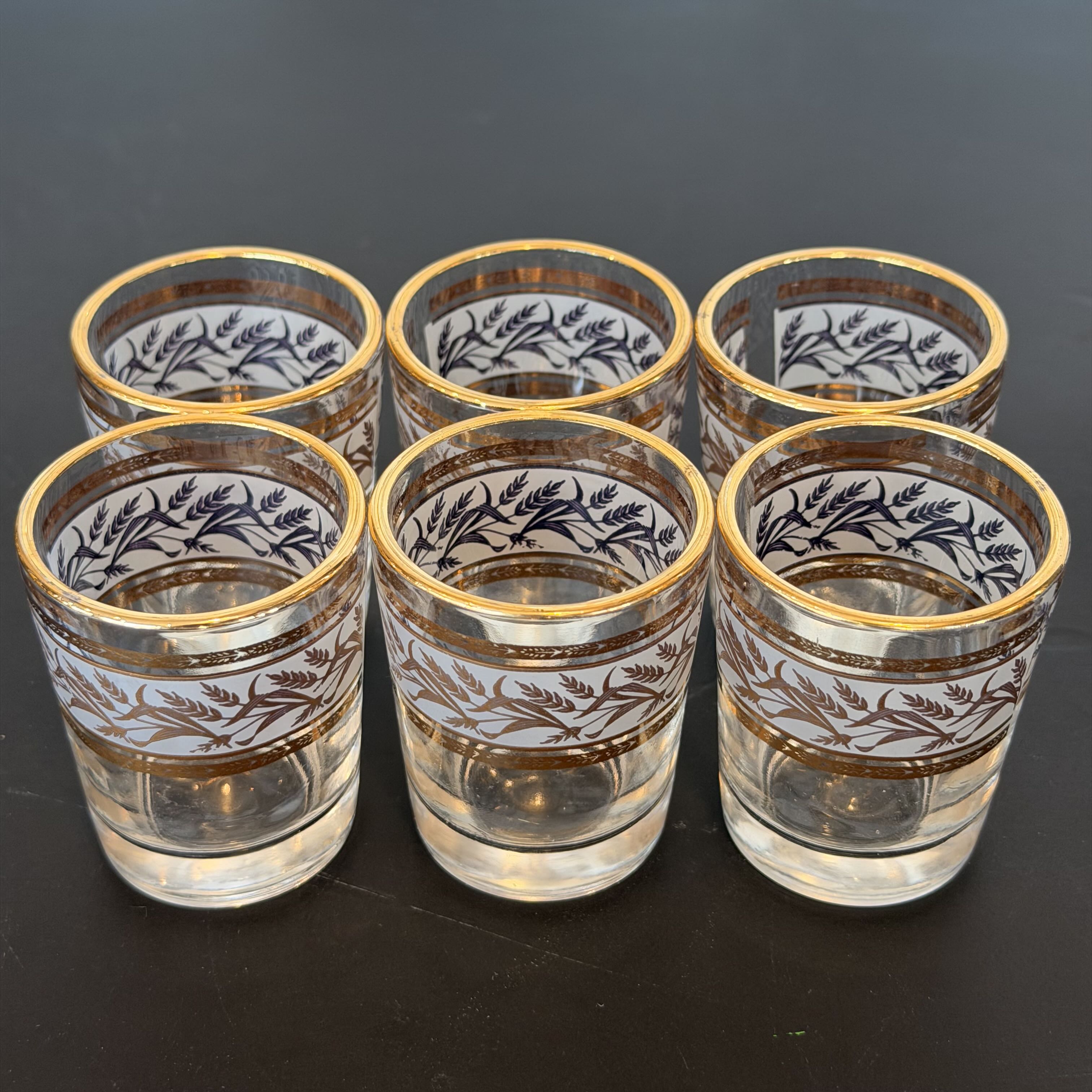 Set of six glass tumblers with gold rims and intricate designs on a dark surface