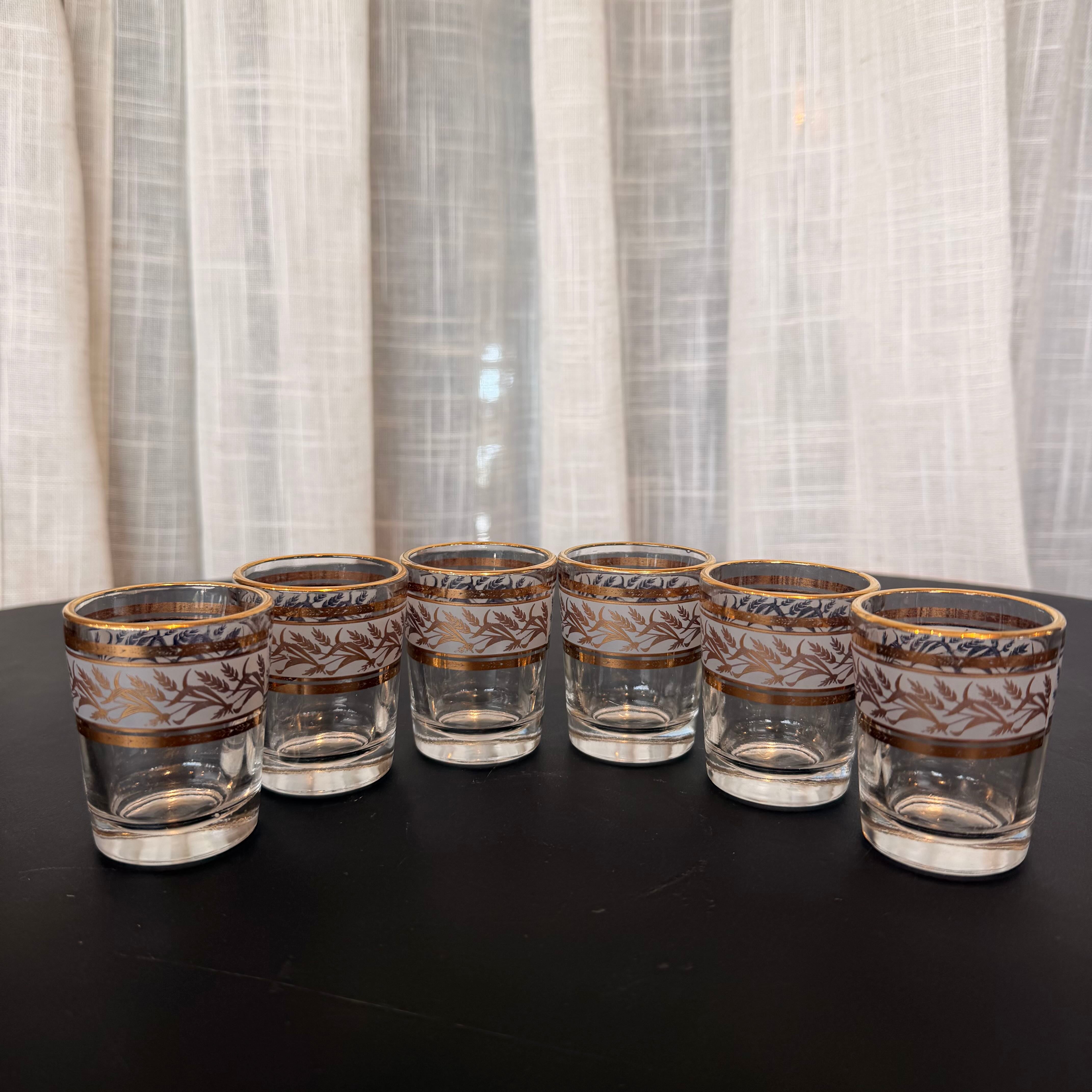 Set of eight glass tumblers with decorative bands on a black surface and white curtain background