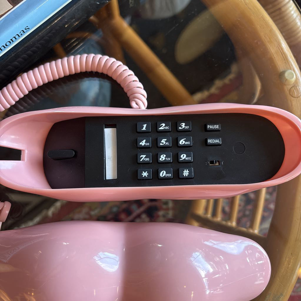 A corded phone of pink lips on a glass table in a room setting.