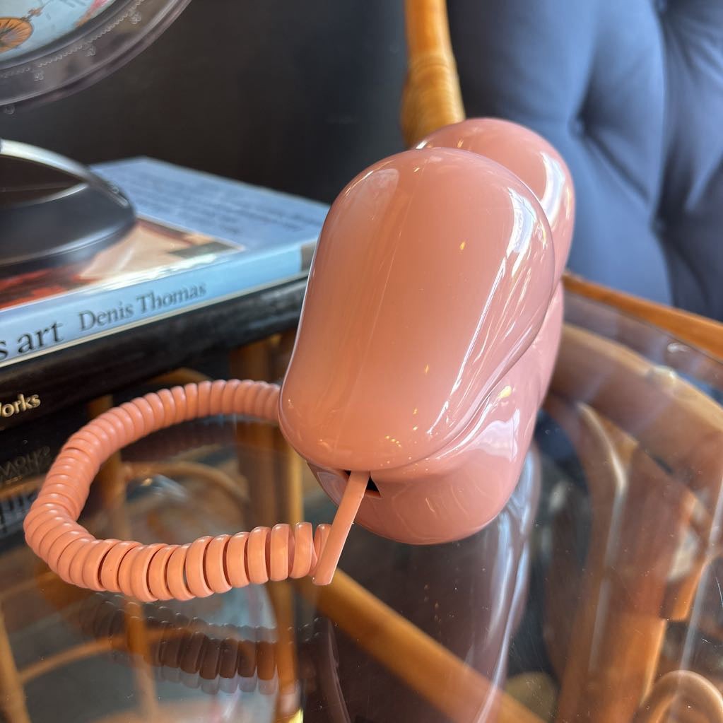 A corded phone of pink lips on a glass table in a room setting.