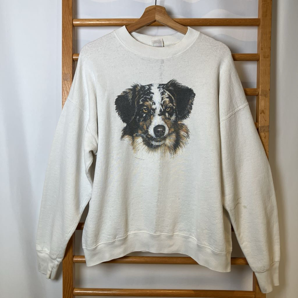 Beige sweatshirt with a dog graphic on a wooden hanger against a white wall.