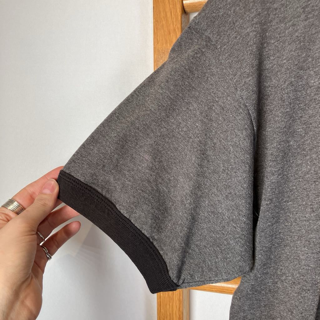 Gray t-shirt with black trim held by a hand against a white background