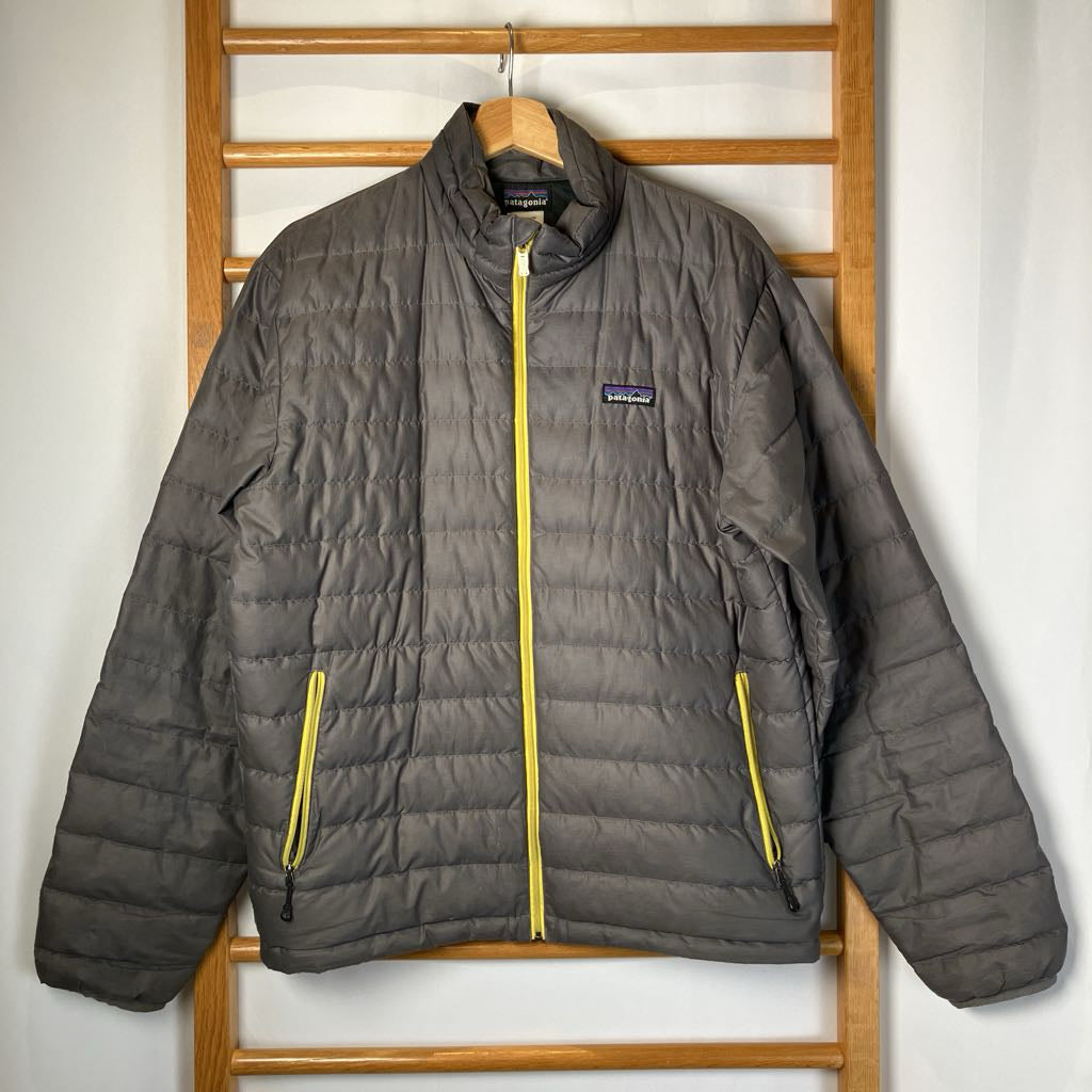 Gray puffer jacket with yellow zippers on a wooden hanger against a white wall.