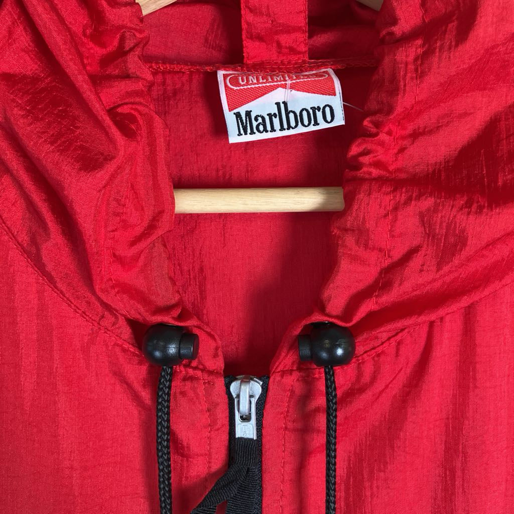Close-up of a red lightweight zip-front garment with black drawstrings and a Marlboro label at the collar, hanging on a wooden hanger.