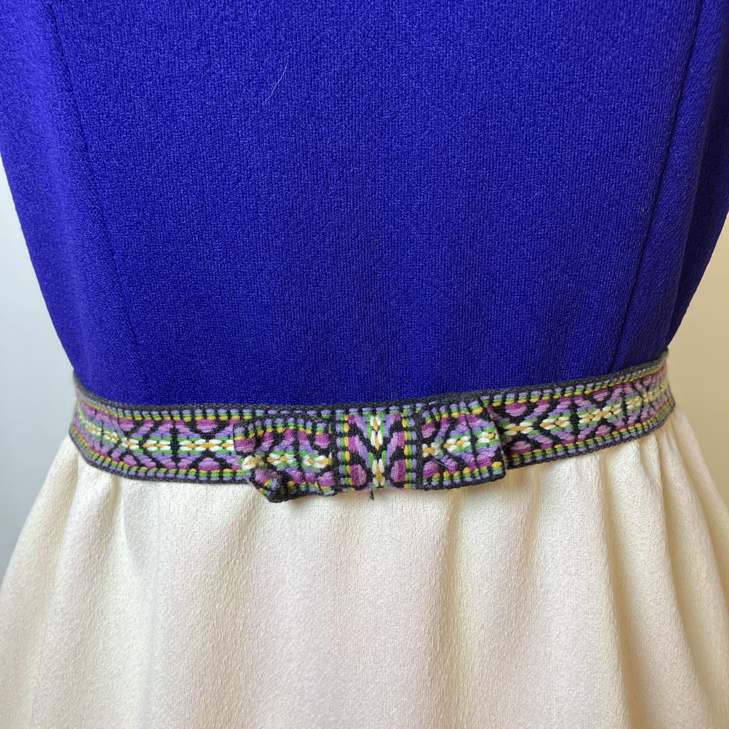 Close-up of a blue top with a decorative belt and beige skirt against a neutral background