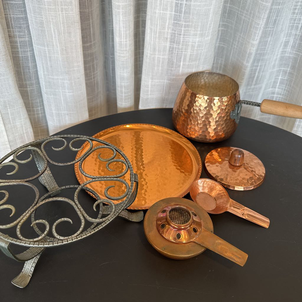 Collection of copper cookware including pots and lids on a dark surface with a light curtain background.