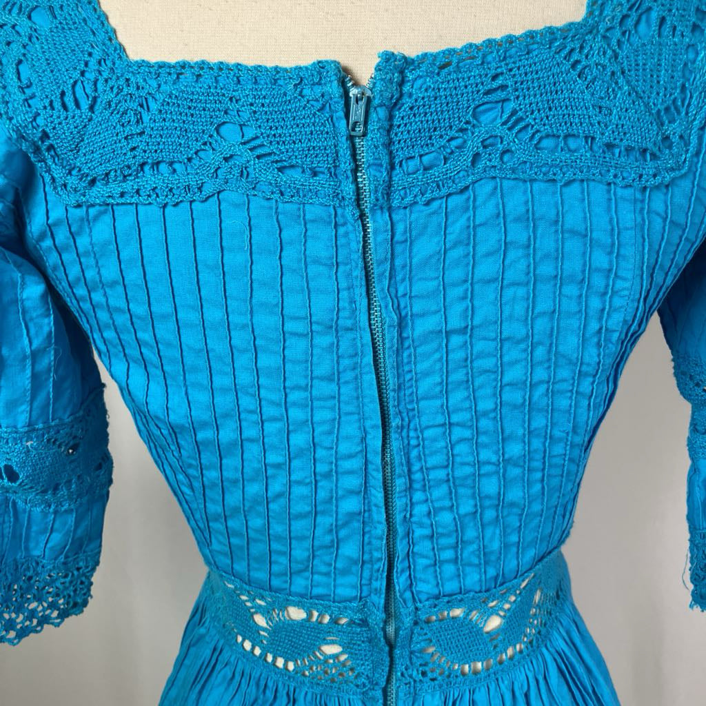 Close-up of a blue dress with intricate lace detailing on a neutral background