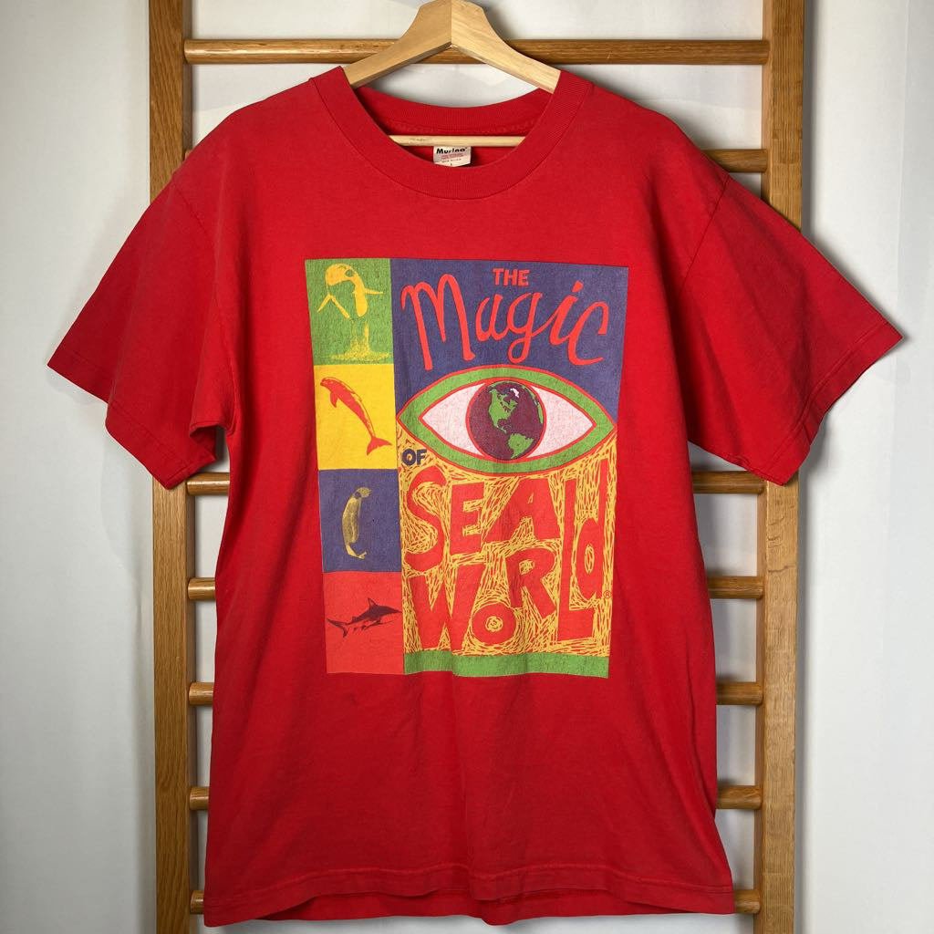 Red t-shirt with colorful graphic design on a wooden hanger against a white wall.