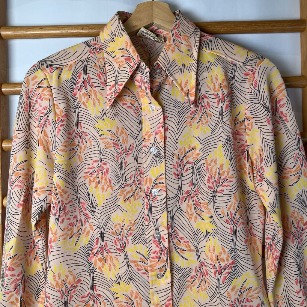Floral patterned shirt on a wooden hanger against a wall.