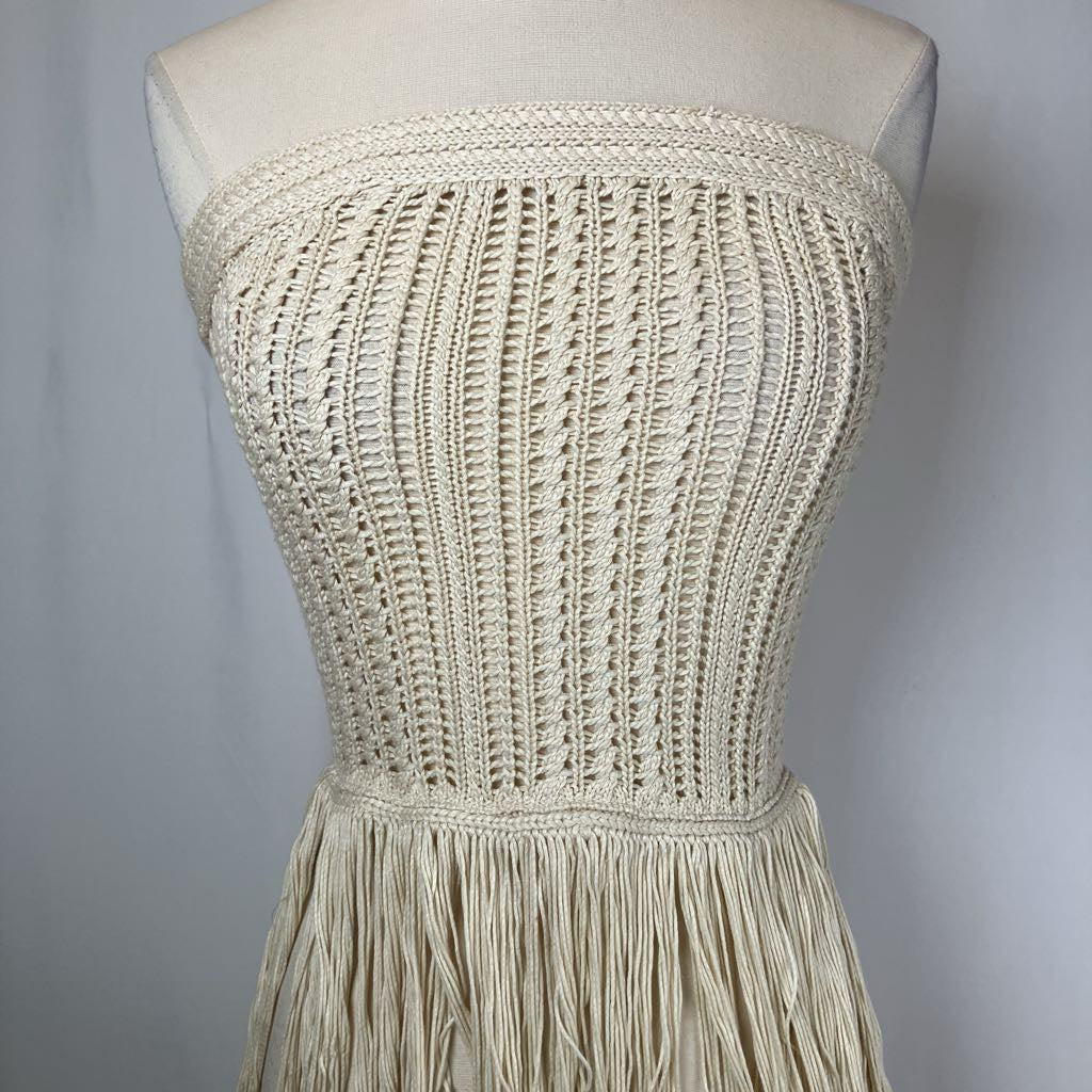 Beige crochet dress with fringe on a mannequin against a gray background