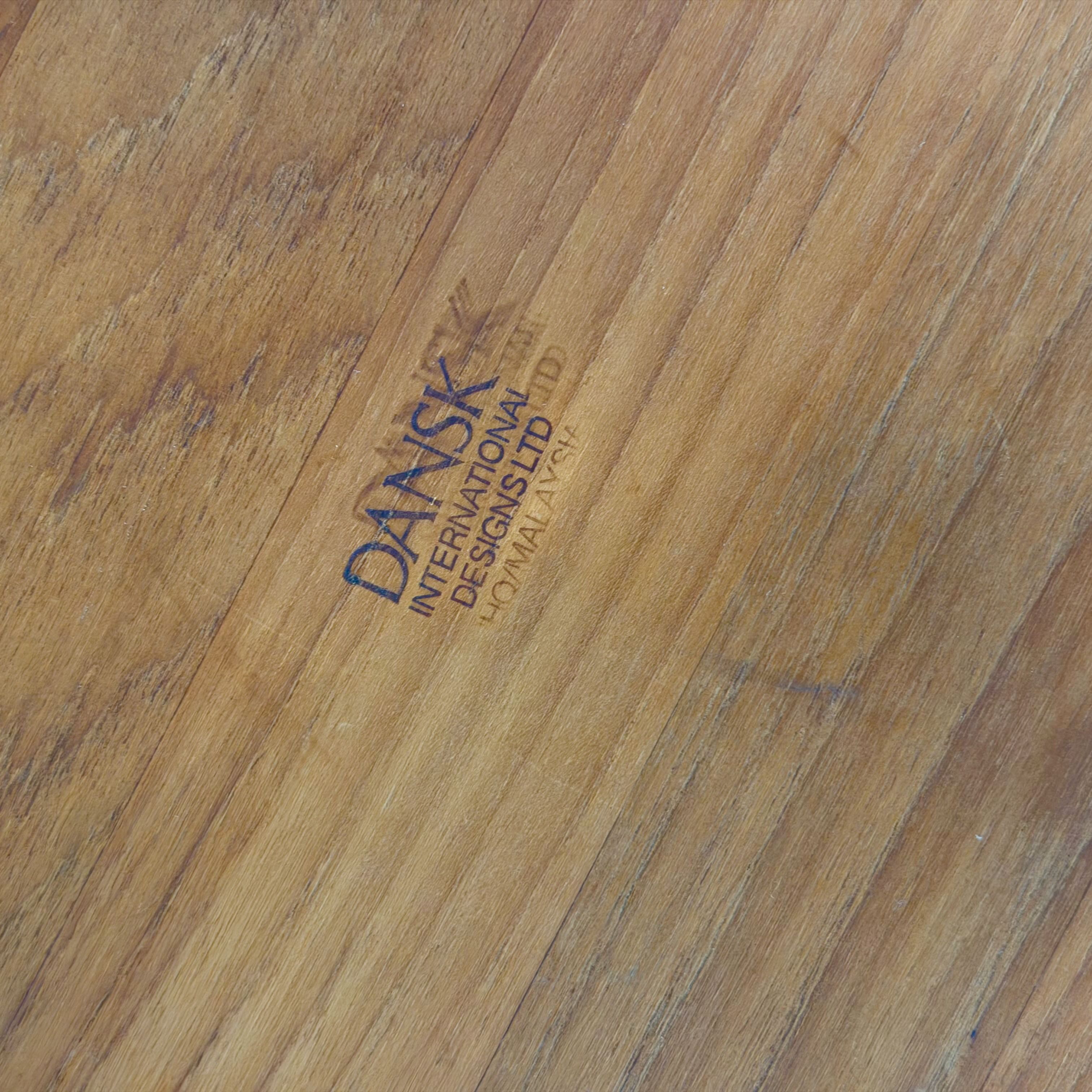 Close-up of a light brown wood grain surface with a stamped logo reading 'DANSK INTERNATIONAL DESIGNS LTD' and 'TOMAS HAVNAR'.