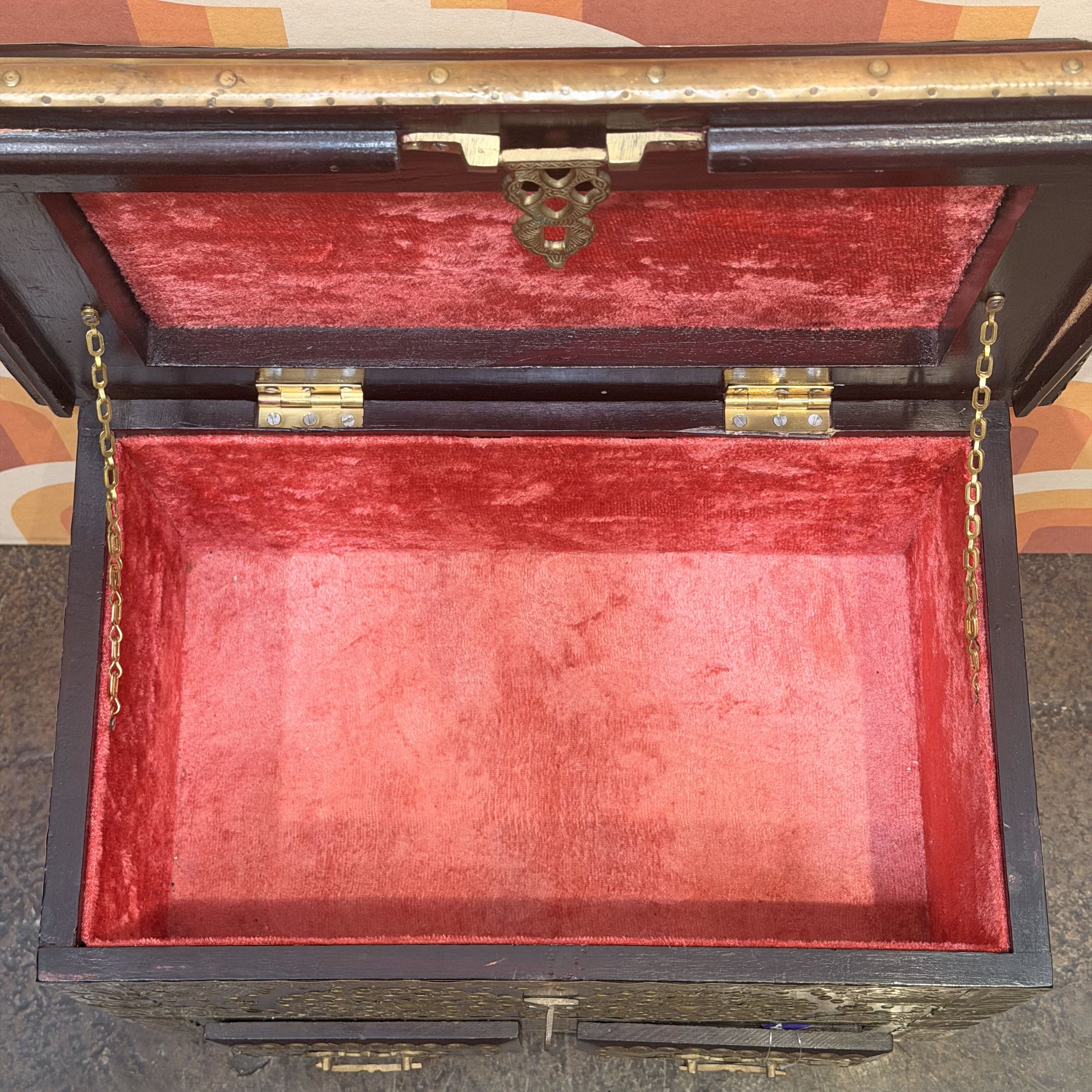 Wooden chest with red interior and brass hardware on a patterned background