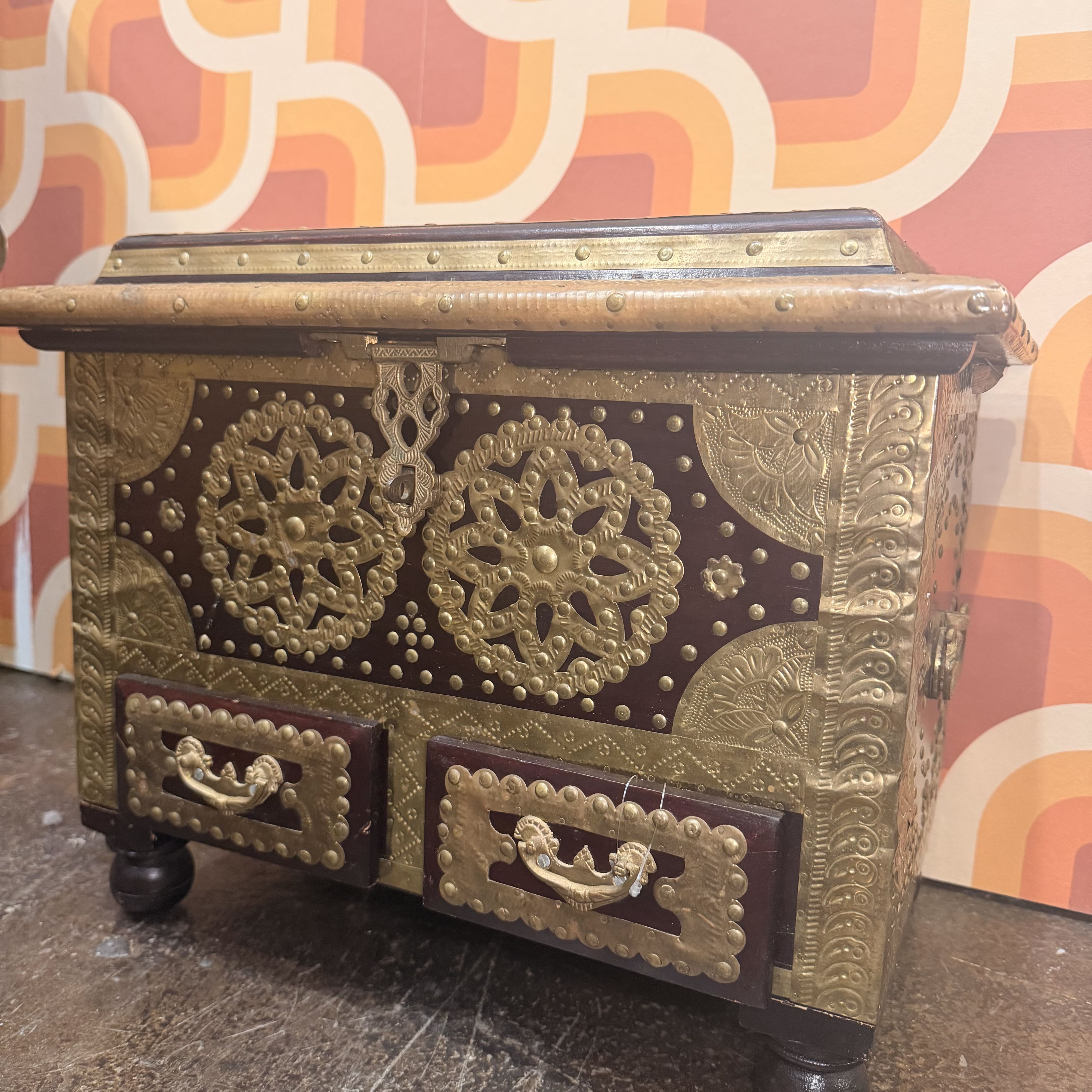 Decorative wooden chest with gold embellishments against a colorful geometric-patterned wall.