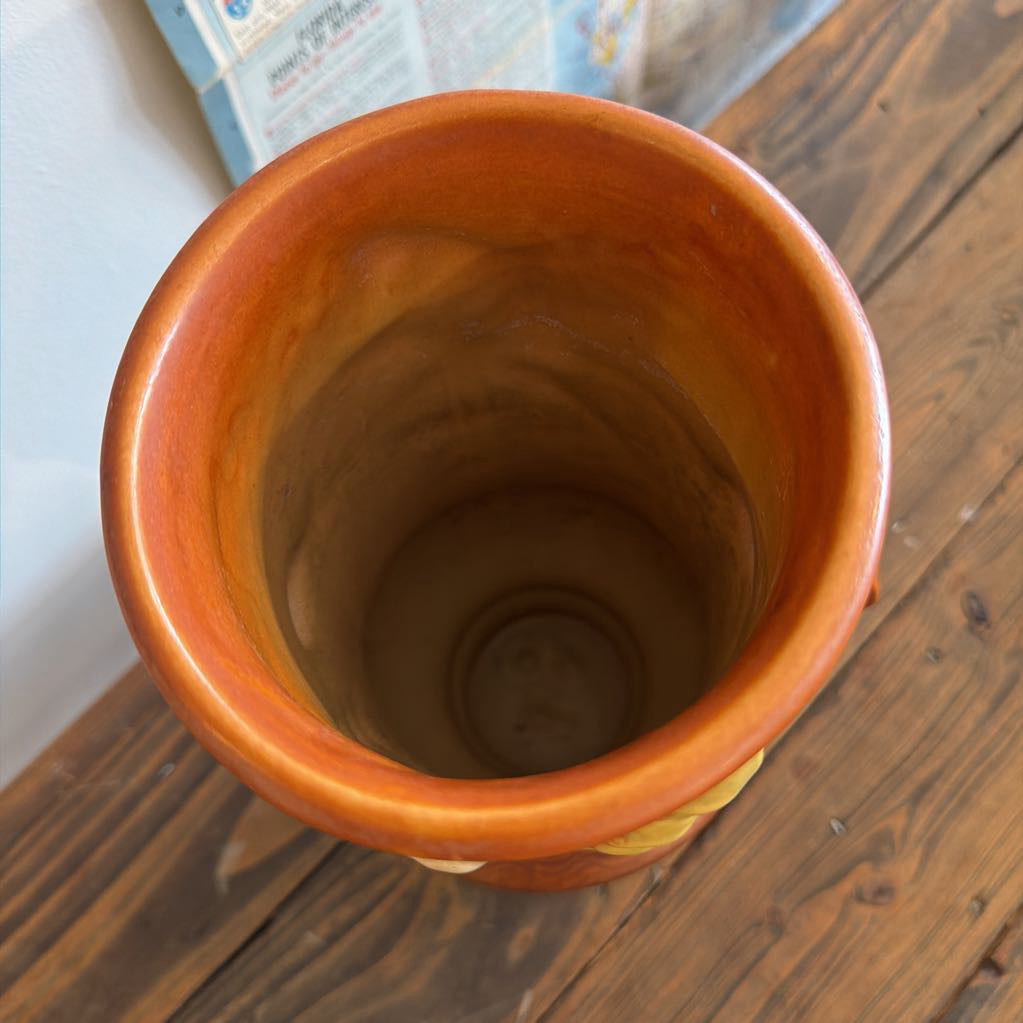 An orange glazed ceramic planter viewed from above, showing its round opening and smooth interior, set on a dark wooden surface.