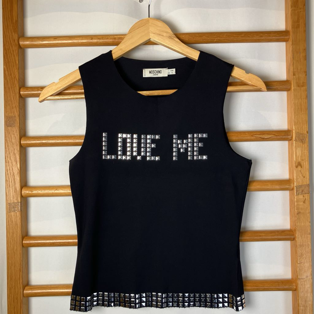Black tank top with 'LOVE ME' text on a wooden hanger against a white wall.