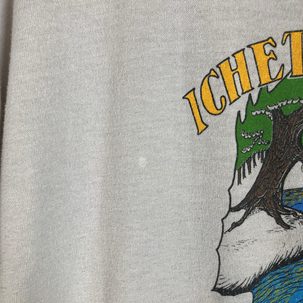 Close-up of a light gray or off-white fabric surface with part of a printed graphic visible on the right side, showing yellow text and a multicolored illustration.