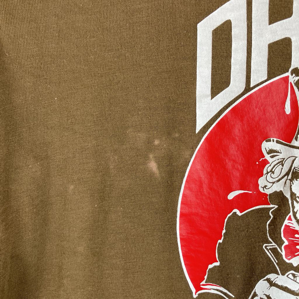 Close-up of a brown graphic t-shirt featuring a red circular design with a stylized character and white lettering.