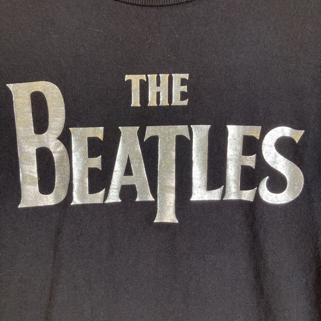 Close-up of a black T-shirt featuring a large metallic silver 'THE BEATLES' logo printed across the chest.